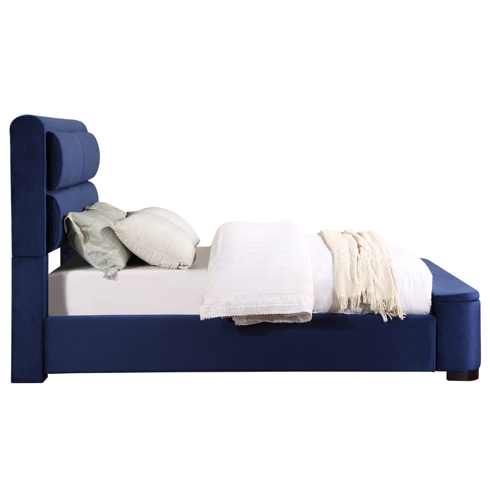 Front-facing side view of a modern glam navy blue upholstered bed with linens on a white background
