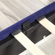 Left-angled close-up frame and underbed drawer detail view of a modern glam navy blue upholstered storage bed with nailhead trim on a woodgrain floor