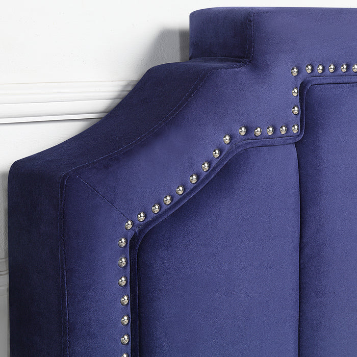 Right-angled close-up headboard detail of a modern glam navy blue upholstered storage bed with nailhead trim against a white wall
