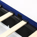 Right-angled close-up frame and underbed drawer detail view of a modern glam navy blue upholstered storage bed with nailhead trim on a white background