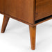 Detailed shot of the tapered and splayed feet of an oak finished mid-century modern style nightstand against a white background.