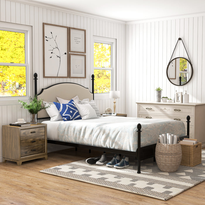 Right-angled Eastern King-sized four-poster bed sits in a white room with slatted walls. The farmhouse design is complete with mixed-style case goods. A wood nightstand sits on the left of the bed, while a beige-tone dresser sits in the background, on the right. Two different toned wicker baskets of different shapes sit at the foot of the bed, while tennis shoes tuck under the bed. Beneath these objects is a beige and black ikat patterned rug.