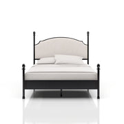 Right-angled California King-sized four-poster bed sits against a white background. The camelback is a beige upholstery while the frame of the bed is a gunmetal finish with slender posts that present ball finials.