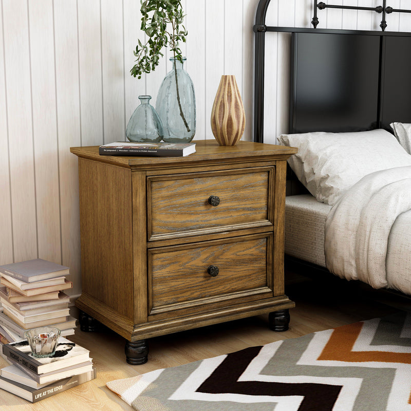 Right-angled oak 2-drawer nightstand in a modern farmhouse-style bedroom. The traditional style design is embellished with knob pulls and black cylindrical feet to tie in with the black metal bed. The white shiplap wall gives a neutral backdrop to the bedroom furnishings.
