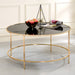 Front-facing contemporary gold and black glass round coffee table in a living room with accessories