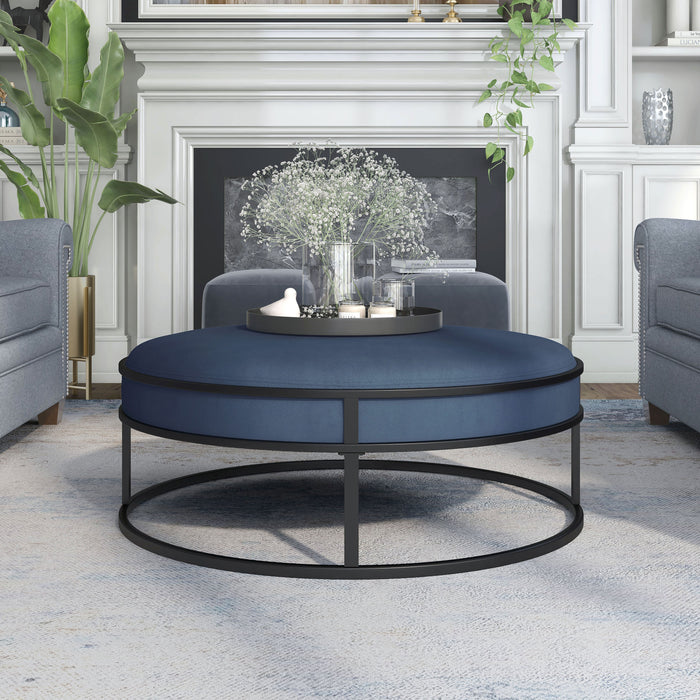 Front-facing contemporary navy and black round ottoman in a living room with accessories