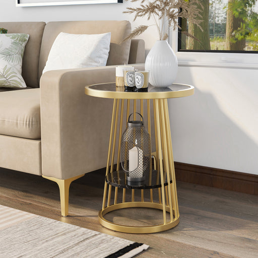 Left angled modern glam round side table with slim gold steel frame and decorated glossy black tabletop and open lower shelf next to a sofa.