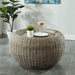 Front-facing coastal woven rattan look round accent table in a c casual living space with accessories