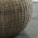 Left-side close up coastal woven rattan look round accent table base detail on a gray tile floor