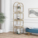 Left-facing modern gold arched bookcase with decor in living room. Four open glass shelves with an open steel frame.