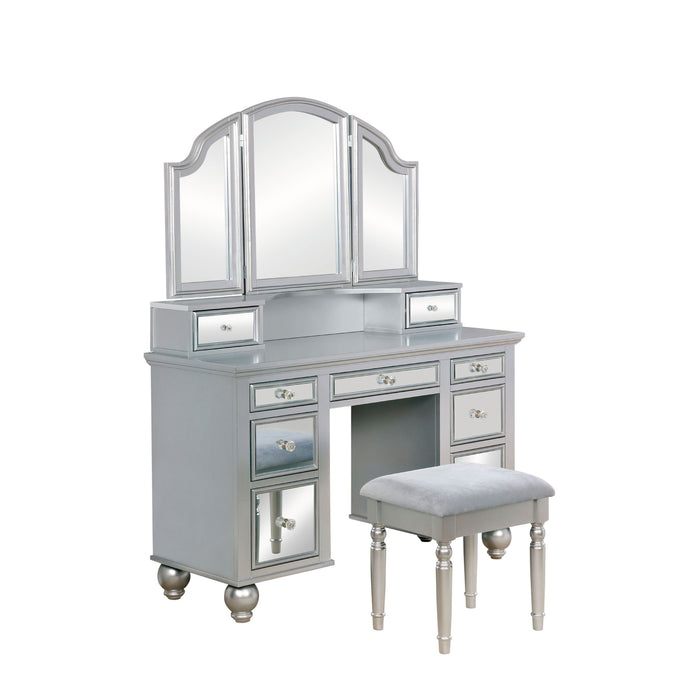 Right-angled silver vanity set against a white background. This vanity table offers a tri-fold mirror and a total of nine mirrored drawers with acrylic knobs. Bun feet hold up the vanity table, while turned legs prop up a fabric-top stool.
