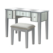 Left-angled silver vanity set against a white background. This vanity table features a mirrored tabletop and stripe frosted mirrored drawers with acrylic knobs. It stands on long tapered legs to match the fabric-top stool.