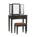 Right-angled black vanity set against a white background. A tri-fold mirror, drawer with silver bar pull, and microfiber upholstered seat sit on tapered legs.