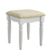 Right-angled white vanity stool against a white background. Turned legs and a curved skirt prop up a fabric-top seat.