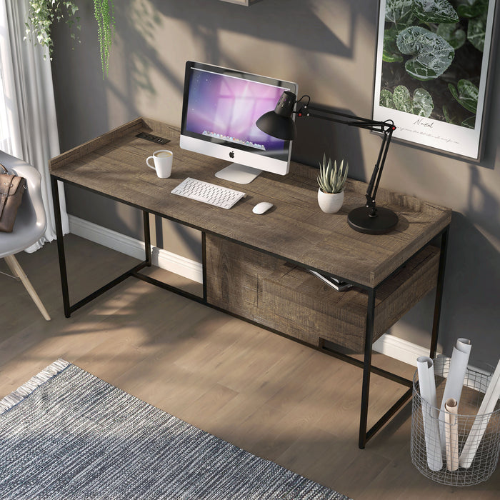 Left angled top view of an industrial one-drawer rustic oak and black writing desk with power outlets and USB ports in a living area with accessories