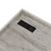 Cropped, angled view of desktop corner and power outlet on industrial light gray and matte black steel and particle board writing desk on white background