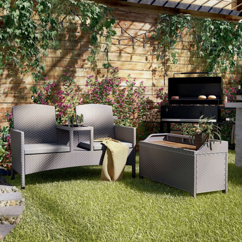 Right-angled light grey wicker outdoor 2-piece loveseat and storage bench set against a white background. The bench is lipped to offer space for a cushion, while the loveseat includes two grey cushions and a black tempered glass built-in center console table.
