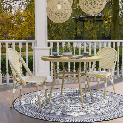 Natural tone and yellow wicker bistro set on a porch. The table sits on a round rug, offering two cups of tea. A chevron pattern wicker adds style to the set.