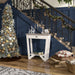 Ivory entryway table with a light oak tabletop at the base of a navy blue staircase. A Christmas Tree with silver and gold ornaments sits on its left while the staircase is adorned with garland.