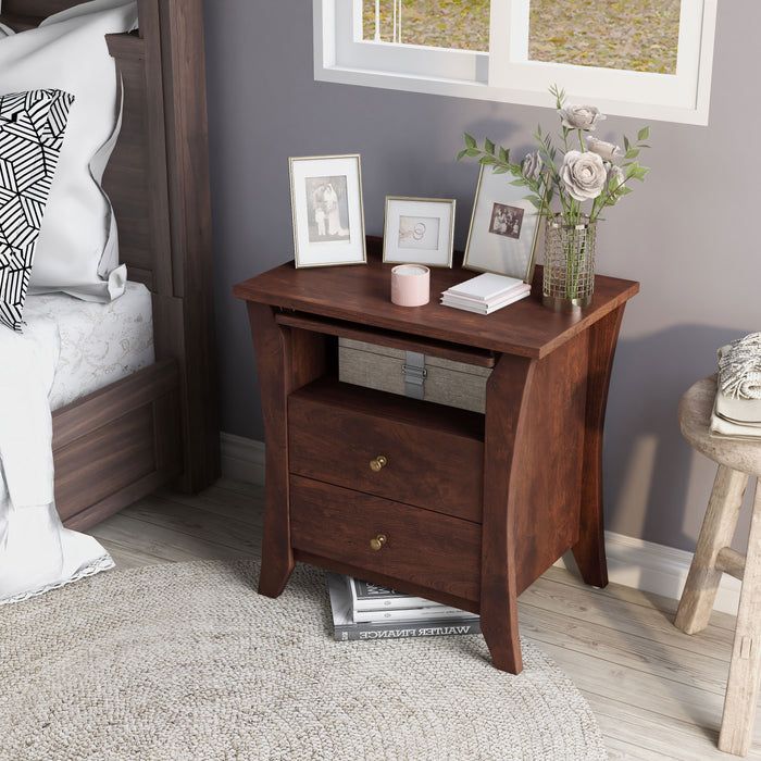 This is a left-angled vintage walnut nightstand in a contemporary bedroom. Curved leg panels create a calming silhouette while copper knobs add class to the two drawers. An open shelf houses a slide-out tray. Champagne picture frames, flowers, and a candle adorn the bedside tabletop.