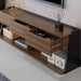 Left angled contemporary three-drawer light walnut and black TV stand with two drawers open in a living area with accessories