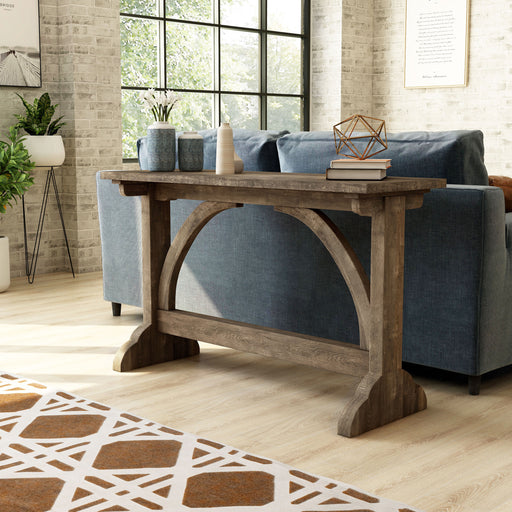 Left-angled rustic reclaimed oak wood finish console table with arch braces against a sofa in a modern farmhouse living space with accessories