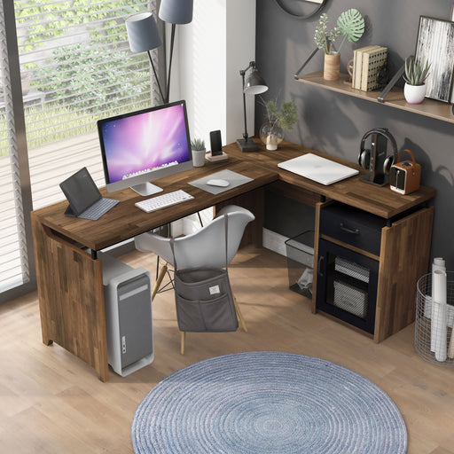 Top view of a light hickory L-shaped desk in an urban home office. The desktop holds electronic devices, a table lamp, and plants. Beneath the desk is a computer and a black wire mesh trash bin to match the cabinet. 