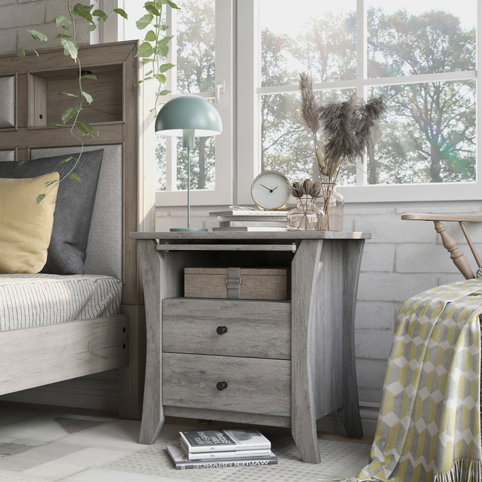 Left-angled transitional vintage gray oak finish wood two-drawer nightstand with flared sides, one fixed shelf, and a pull-out shelf in a modern farmhouse bedroom with accessories