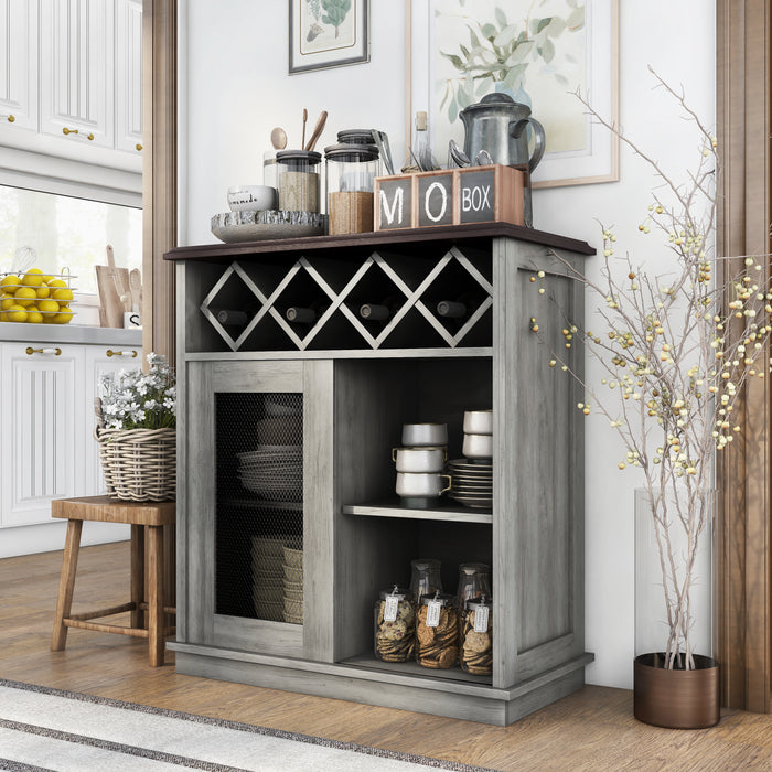 Left-angled vintage grey oak wine buffet against a white wall. Baking supplies present themselves on the tabletop while the lattice wine rack holds four bottles. On the open shelves are dishes and cookie jars. To the left of the server is a stool holding a basket of flowers. The background is a traditional kitchen with white cabinets and counters displaying lemons and cutting boards.