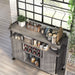 Top view of a vintage grey oak wine cabinet in an urban loft. It sits on a taupe wood floor against a white brick wall, under a black-framed window. The pipe-accented lipped top displays silverware while the open shelves store other kitchen supplies. The wine rack holds 8-bottles.